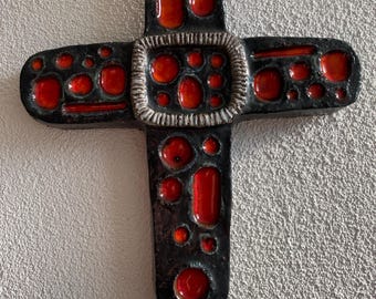 May include: A black and red ceramic cross with a textured surface. The cross has a silver-colored border around the center.