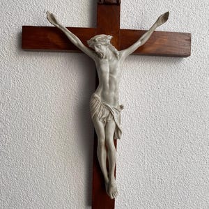 Può includere: Un crocifisso di legno con una figura di Gesù bianca. La figura ha le braccia distese e indossa una corona di spine. Il crocifisso è montato su una parete bianca.