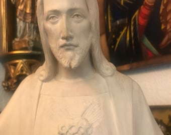 May include: A white plaster statue of Jesus Christ with a heart on his chest. The heart is surrounded by thorns and rays of light.