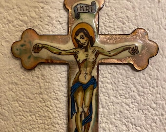 Może przedstawiać: Miedziany krucyfiks z namalowanym wizerunkiem Jezusa Chrystusa na krzyżu. Krzyż jest ozdobiony patyną w kolorze złotym, a napis "INRI" jest namalowany na niebieskim banerze nad głową Jezusa.