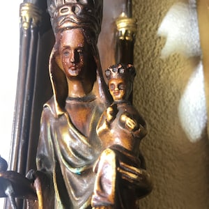 Puede incluir: Una escultura de madera de la Virgen María y el niño Jesús. La escultura está pintada en tonos marrones, dorados y azules. La Virgen María lleva una corona y una túnica azul. El niño Jesús está sentado en su regazo y lleva una túnica blanca.