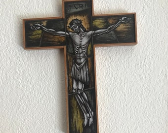 Może przedstawiać: Drewniany, oprawiony krucyfiks ze szkła witrażowego z przedstawieniem Jezusa Chrystusa na krzyżu. Szkło jest w odcieniach brązu, żółci i czerni.