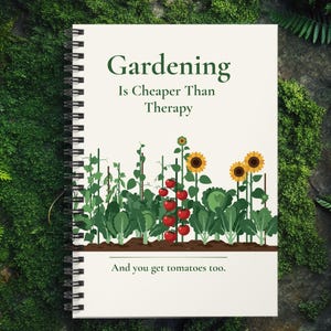 Peut inclure: Un carnet à spirales avec le texte "Gardening Is Cheaper Than Therapy" et "And you get tomatoes too." La couverture présente une illustration de jardin avec des tomates et des tournesols. Le carnet repose sur une surface verte et mousseuse.