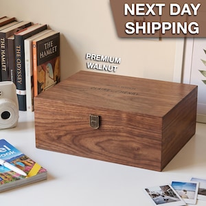 May include: A rectangular walnut wood keepsake box with a hinged lid and a metal latch. The lid is engraved with the text "PRECIOUS MEMORIES CLAIRE AND HENRY EST. 2018". The box has a visible wood grain pattern and a smooth, dark brown finish.