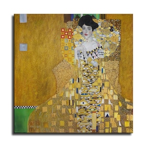 Puede incluir: Impresión enmarcada de una pintura de Gustav Klimt. La obra presenta a una mujer con un vestido largo y ornamentado con patrones geométricos y detalles dorados. El fondo es de color oro intenso, y la mujer tiene un moño oscuro.