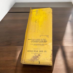 May include: A yellow metal shoe size measuring tool with a ruler and instructions. The tool is labeled "Double-Wear Shoe Co. Minneapolis, Minn."