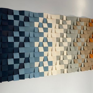 May include: A wall art piece made of wood with a geometric pattern. The piece is made up of squares and triangles in shades of blue, white, gray, and orange.