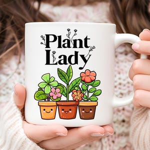 Peut inclure: Une tasse en c&eacute;ramique blanche avec le texte "Plant Lady" en lettres noires. La tasse pr&eacute;sente une illustration de trois plantes en pot avec des visages souriants.