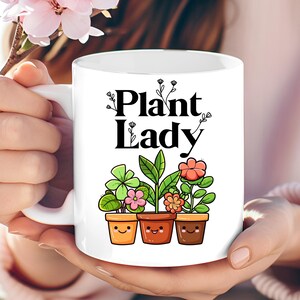 Peut inclure: Une tasse en c&eacute;ramique blanche avec un motif noir qui dit "Plant Lady" et repr&eacute;sente trois plantes en pot avec des visages souriants.