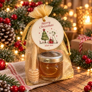 May include: A gold organza drawstring bag containing a small glass jar of honey and a wooden honey dipper. A round tag attached to the bag features the text Merry Christmas and With love, with an illustration of a Christmas tree and a dog.