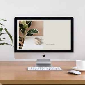 May include: A desktop computer with a white background and the text "Today is a new day." displayed on the screen. A potted plant and a ceramic mug are visible on the desk.