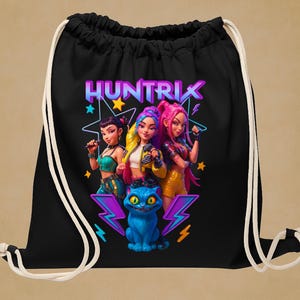 Peut inclure: Sac de sport noir avec un graphisme vibrant de trois femmes stylisées et d'un chat bleu aux yeux brillants. Le mot "HUNTRIX" est affiché en couleurs néon au-dessus des personnages. Des cordons blancs complètent le design.