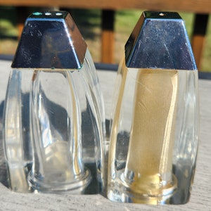 May include: Two clear glass salt and pepper shakers with silver tops. The shakers are on a wooden surface.