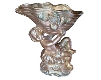 May include: A gold cherub figurine holding a shell-shaped dish. The cherub is sitting on a base with ornate details.
