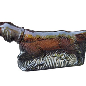 May include: A brown glass bottle shaped like a running dog. The bottle has a textured surface and is decorated with a floral design.