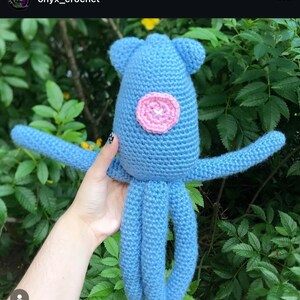 May include: A crocheted blue octopus with a pink circle in the centre of its body. The octopus has eight tentacles.