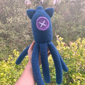 May include: A crocheted blue octopus plush toy with a purple button with a white X on it.
