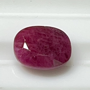 Może przedstawiać: Fasetowany, owalny kamień szlachetny rubinu. Klejnot ma głęboki, bogaty czerwony kolor z wypolerowaną powierzchnią. Rubin jest umieszczony na białym tle.