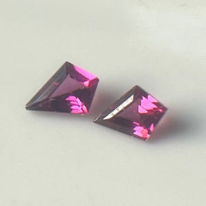 Könnte beinhalten: Zwei facettierte, trapezförmige Edelsteine in tiefem Magenta. Die Edelsteine haben eine polierte Oberfläche und sind vor einem weißen Hintergrund platziert. Die Steine sind wahrscheinlich für die Schmuckherstellung oder zum Sammeln gedacht.