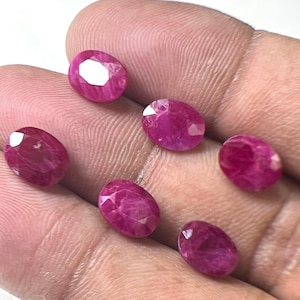 Puede incluir: Siete rubíes de corte ovalado en tonos rosados y rojizos. Las piedras preciosas están facetadas, reflejando la luz y mostrando su estructura interna. Los rubíes se exhiben sobre un fondo neutro.