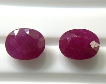 Puede incluir: Dos rubíes facetados de forma ovalada con un color rojo magenta profundo y saturado. Cada piedra preciosa presenta una superficie pulida con múltiples facetas geométricas que reflejan la luz, mostrando una calidad translúcida.