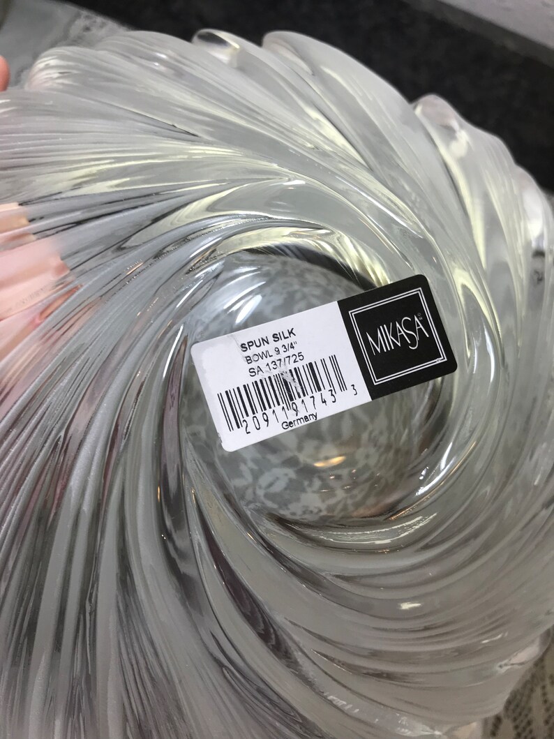 Puede incluir: Un cuenco de vidrio transparente con un dise&ntilde;o en espiral. El cuenco est&aacute; etiquetado con "SPUN SILK BOWL 9 3/4" y "SA 137/725" con un c&oacute;digo de barras y "Alemania" impreso en la etiqueta. La etiqueta tambi&eacute;n incluye el logotipo de Mikasa.