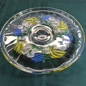 May include: A clear glass serving dish with a raised rim and a central dip. The dish features a hand-painted design of yellow bananas, blue grapes, and white flowers.