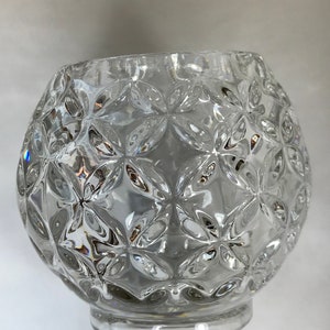 May include: A clear glass candle holder with a decorative, textured pattern of small flowers. The holder has a round base and a wide, open top.