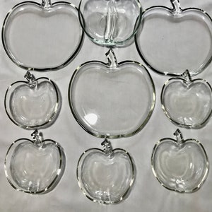 May include: Set of nine clear glass apple-shaped serving dishes. The set includes a large bowl, two medium-sized bowls, and six small bowls.