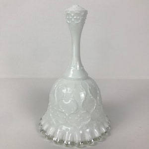 May include: A white milk glass bell with a scalloped edge and a delicate floral design. The bell has a silver trim around the bottom edge.