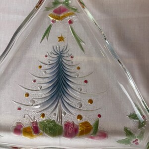 May include: A clear glass triangular serving platter with a Christmas tree design. The tree is blue and silver with red, gold, and clear ornaments. Presents and holly are at the base. Gold bells and a star are at the top.