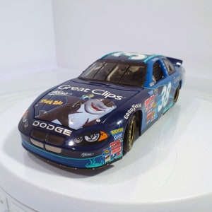 Op de afbeelding: Een marineblauwe Dodge raceauto speelgoed met het nummer 38 aan de zijkant en op het dak. De auto heeft het "Great Clips" logo en een cartoon haai grafiek uit de film "Shark Tale". De auto heeft sponsorstickers en een zwart interieur.