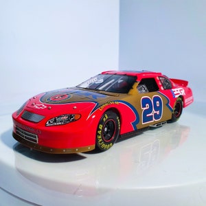 Op de afbeelding: Een rood, goud en blauw raceauto model met het nummer 29 aan de zijkant. De auto heeft sponsorlogo's en Goodyear banden. Het model is een gedetailleerde replica van een NASCAR-voertuig.