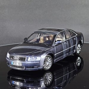 May include: A dark blue die-cast model car with chrome wheels and a sunroof. The model car has a detailed interior and is reflected in the glossy black surface below. The license plate reads "M-CZ 923".