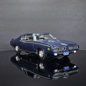 Puede incluir: Modelo a escala azul oscuro de un coche GTO clásico. El modelo presenta ruedas cromadas, un interior detallado y franjas amarillas de carreras. La matrícula dice "10W-218".