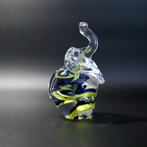 May include: A decorative glass elephant figurine. The elephant has a curled trunk and is made of clear glass. The body is swirled with blue, yellow, and green colours. A small ornament for display.