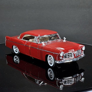 Puede incluir: Modelo de coche clásico rojo con neumáticos de banda blanca. El coche tiene una parrilla y molduras cromadas, y un techo rígido rojo. Es una réplica de un vehículo antiguo, probablemente de mediados del siglo XX.