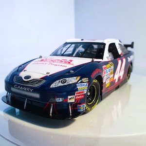 Op de afbeelding: Een blauw, wit en rood Toyota Camry raceauto model. De auto heeft nummer 44 op de zijkant en diverse sponsorlogo's. De motorkap toont de tekst "Literacy Program". De auto heeft zwarte banden en een voorspoiler.