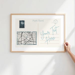 Könnte beinhalten: Ein gerahmter Postkartendruck mit einem hellen Holzrahmen. Die Postkarte zeigt ein Kartendesign, Briefmarken und den Text "Post Card" und "Your Text Here" in einer handschriftlichen Schriftart. Der Druck wird vor einer weißen Wand angezeigt.