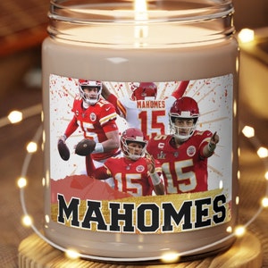May include: A brown glass candle jar with a white label featuring a collage of photos of a football player wearing a red and white jersey with the number 15. The label also includes the text "Mahomes" in gold lettering.