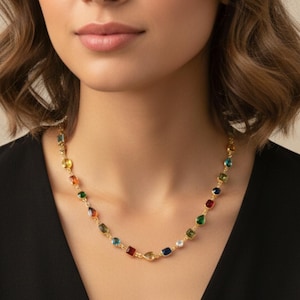 Può includere: Una collana dorata con una serie di pietre preziose quadrate multicolori. La collana è indossata su un top nero. L'immagine è generata al computer e serve solo a dare un'idea di come apparirà la collana quando indossata.