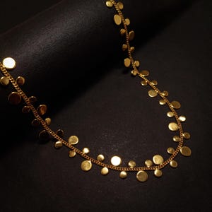 Peut inclure: Un collier en or avec une chaîne et des breloques rondes et plates en or de différentes tailles.