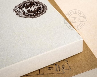 May include: Close-up of two stacked notebooks. The top notebook is off-white with a brown circular emblem that reads "Civilian Conservation Corps" and the years 1933 and 1942. The bottom notebook is brown with a map design.