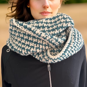 Peut inclure: Une écharpe infinie en crochet bleu sarcelle et crème. L'écharpe est pliée en deux et portée autour du cou.