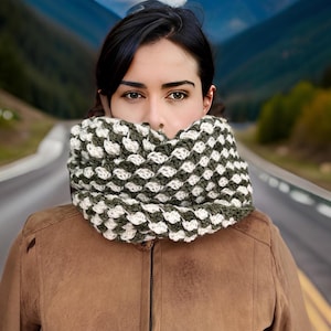 May include: A woman wearing a brown leather jacket with a white and green crocheted infinity scarf.