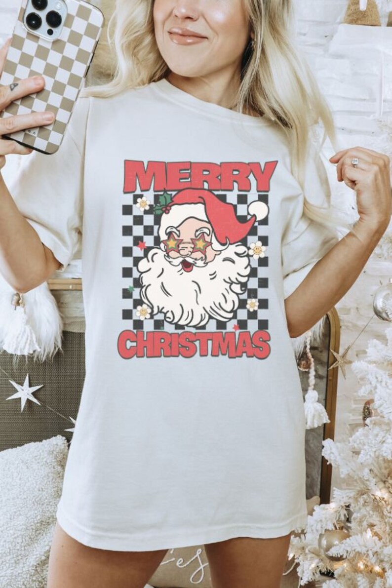 K&ouml;nnte beinhalten: Wei&szlig;es T-Shirt mit einem rot-wei&szlig; karierten Hintergrund, einem Cartoon-Weihnachtsmann mit Sonnenbrille und dem Text "Frohe Weihnachten".