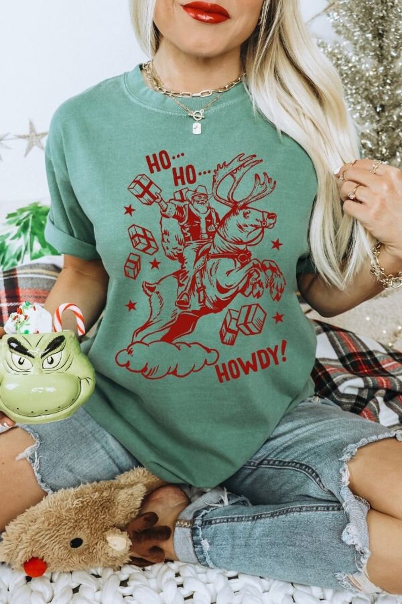 May include: A green t-shirt with a red graphic of Santa Claus riding a reindeer with the text "Ho... Ho... Howdy!"