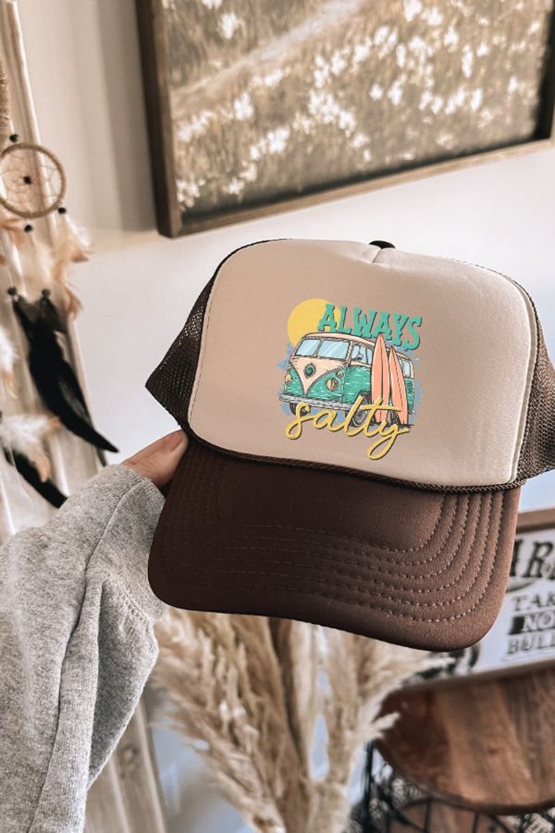May include: A brown and beige trucker hat with a white van and surfboards graphic. The text "Always Salty" is printed on the hat.