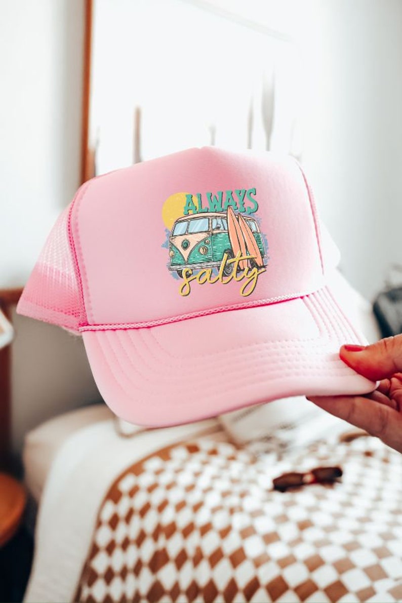 May include: Pink trucker hat with a white mesh back. The front of the hat features a graphic of a vintage van with surfboards and the text "Always Salty".