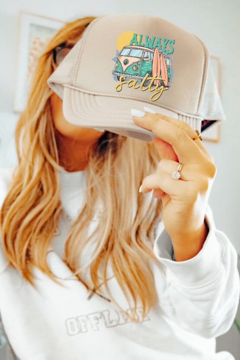 May include: A beige trucker hat with a white and green graphic of a vintage van with surfboards and the text "Always Salty".